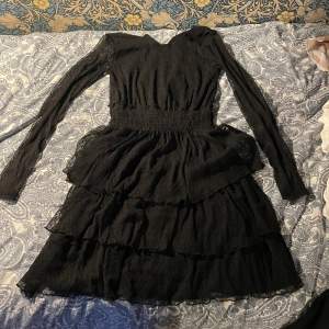 Det är en svart klänning i polyester med lite volang i bra skick