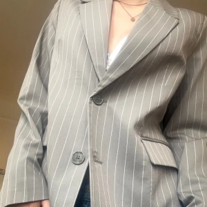 Grå/vit randig kavaj/blazer - En superfin oversized kavajmed axelvaddering i en härlig grå färg från Bik Bok!💗 Endast använd en gång, så som ny. Väldigt fin knäppt med en spetstopp under och en kort kjol!! Pris är prutbart!!🙌(sitter bra på mig som S men funkar säkert till M)