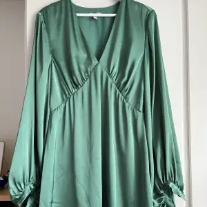 Smaragdgrön satinklänning med stora ballongärmar. Klänningen är ganska kort, typ mitt på låret på mig som är knappt 170 cm lång. Väldigt vackert fall! Använd en gång. 