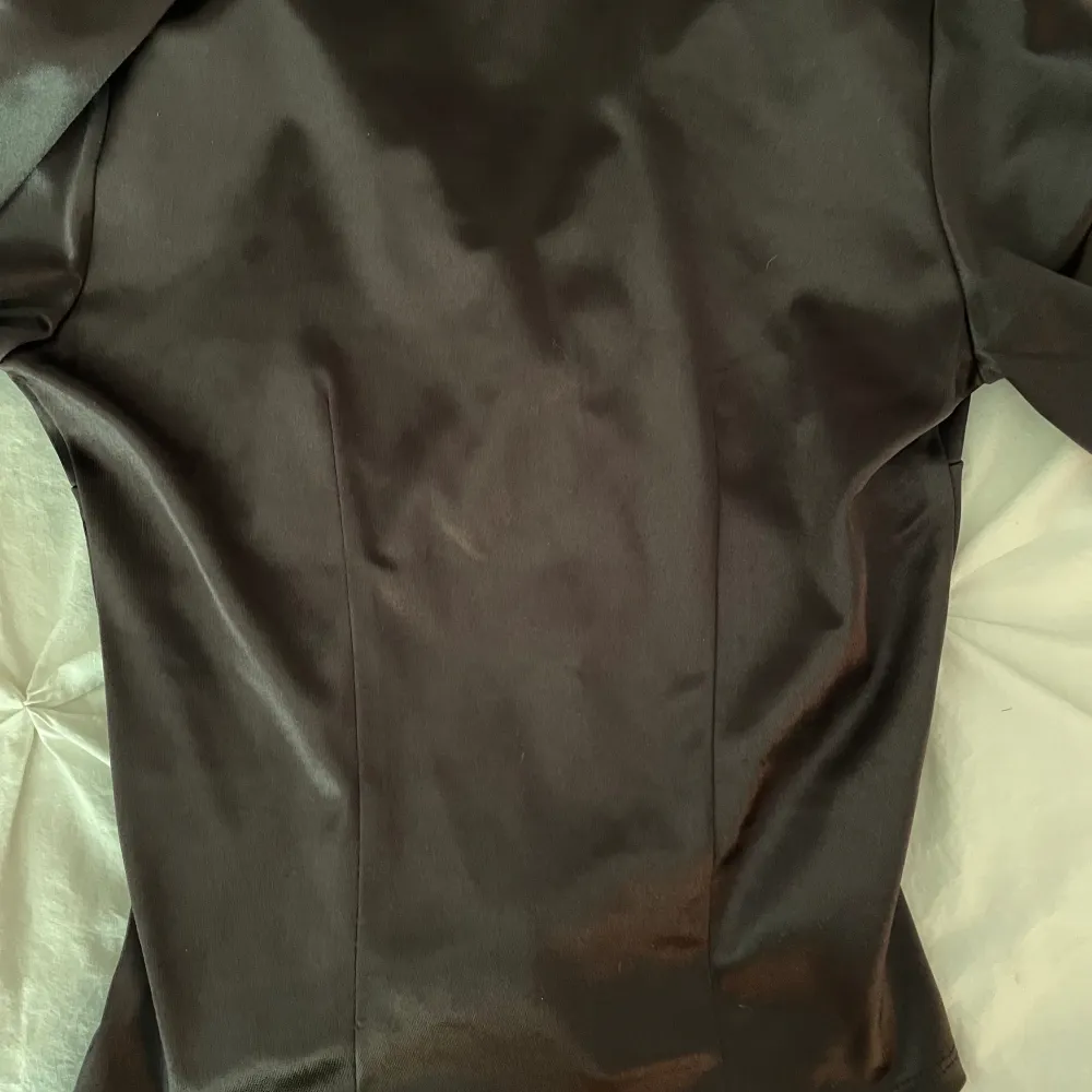 En oanvänd blus/skjorta från H&M i svart/mörkbrun nyans. Satin liknande material, storlek XS. Plagget har en ganska figurnära passform. . Blusar.