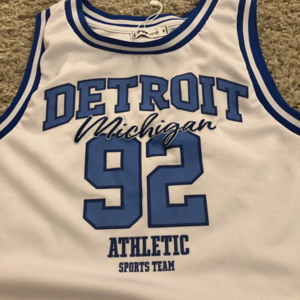 White basketball top with blue text. Toppar.