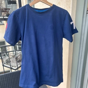 Sail Racing Boys Tee, size 170cm - Enkel marinblå tischa från Sail Racing, med borttagen logga på framsida då den höll på att ramla av, annars i väldigt gott skick. Killstorlek 170cm, men funkar även som en X-small herrstorlek. Köpt på Kidsbrandstore för 499kr. Kan mötas i Sthlm!