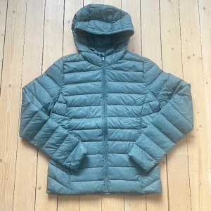 Tunn dunjacka Cubus - Lätt, skön dunjacka med luva från Cubus, i nyskick ej använd. Fin grön/grå/blå färg. Två fickor med dragkedja.  Normal passform och storlek.  Nypris 899 kr