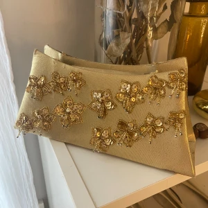 Guldig clutch med blommor - Hade denna fina clutch på min bal (se sista bild) men kommer inte mer till användning, lite smutsig inuti o har klippt av banden som kom till
