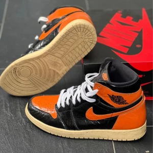Jordan 1 High shattered backboard 3.0 - Använda fåtal gånger. Mycket bra skick. Storlek 43. Orangea, vita och svarta skosnören följer med. Original förpackning. Pris kan diskuteras