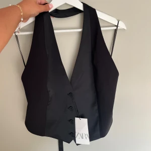 Kostymväst halterneck topp med öppen rygg - Super fin kostymväst halterneck topp med öppen rygg! Justerbar (bild 3) och helt oanvänd med prislapp kvar. Storlek L men för mig som har storlek S/M sitter den bra. Hör av er om ni vill ha bild på hur den sitter på! 