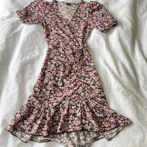 Blommig klänning - Superfin blommig klänning från Gina tricot. Fint skick och är bara använd några få gånger. Har en påsydd knapp (bild 2) men den är enkel att sprätta upp om man inte vill ha den 