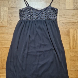 Svart klänning - Svart klänning från Fashionmob i strl M. Glansig överdel med detaljer och resår samt flowy kjol. Gått en tråd fram på kjolen, därav lågt pris, annars fin. Katt i hemmet. 