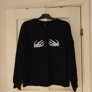 Sweatshirt med tryck  - Sweatshirt med skelett händer som tryck Använd få gånger, i gott skick Lite tunnare material än vad en huvtröja brukar ha Den har XL som storlek men skulle säga den är lite liten i storleken så mer åt L
