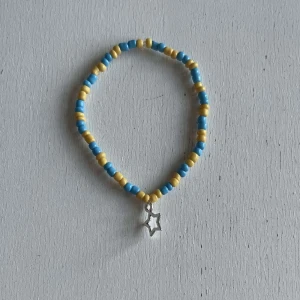 Egengjorda armband - Ett egengjort pärlarmband med färgerna blå, gul och silver. Armbandet har en berlock i silver som avbildar en stjärna. 
