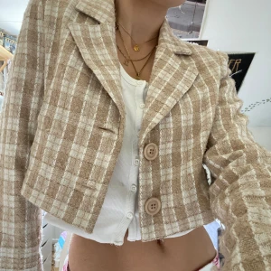 Croppad kavaj - Stilren croppad kavaj från na-kd! Rutigt mönster med vit och beige . Fint men använt skick, en gnutta noppig men det märks inte! Står 36 men åt det mindre hållet (nypris 430)