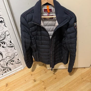 Parajumpers dun lättviktsjacka  - en klassisk och sportig jacka. den ikoniska Parajumper-patchen på vänster axel. Med en högre krage och en tvåvägsdragkedja framtill erbjuder denna både stil och funktionalitet. I nyskick. Kemtvättat. XXL mindre i storlek passar L/XL