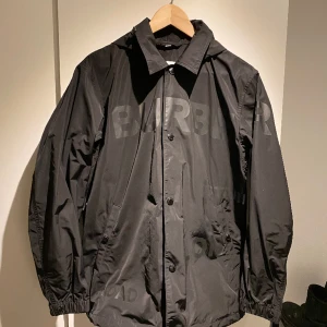 Burberry Regn/Vind Jacka - Burberry Vind / regn Jacka, m Luva och knappar. Har även en Krage för uppknäppt användning. Svart m svarta logotyper Köpt för 2 år sen, använd väldigt sällan, Bra skick! Äkthetsbevis- Kvitton/Tvättlapp finns på begäran   Ursprungspris 9,900kr