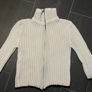 Stickad kofta - Stickad vit kofta/tröja med svarta detaljer. Skulle säga att den passar allt från 36-40.