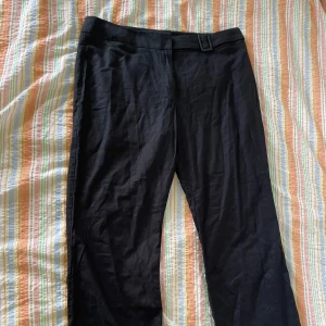 Svarta byxor från Marks & Spencer - Ett par svarta byxor från Marks & Spencer. Byxorna har en enkel design med en dekorativ spänne vid midjan.