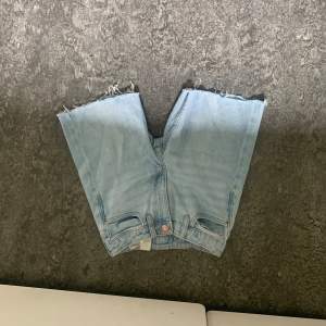 Ett par ljusblå jeansshorts med råa kanter. Shortsen har en klassisk femficksdesign och är tillverkade i denim.