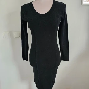 Svart klänning från Hot Zone - En elegant svart klänning från Hot Zone med långärmad design och en tight passform. Klänningen har en rund halsringning och är tillverkad i ett stretchigt material som framhäver figuren. Mindre skönhetsfel i tyget.