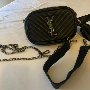 Yves Saint Laurent väska  - En svart Yves Saint Laurent väska med extra tillbehör. Kan anvandas vid flera tillfallen som t.ex ut med vänner eller en special dag.
