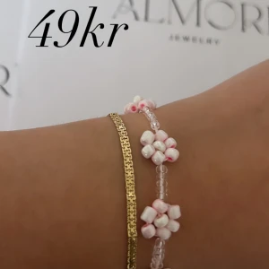 Armband med blommor och guldkedja - Ett vackert armband med små vita och rosa blommor. Armbandet är elegant och passar perfekt för olika tillfällen.