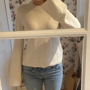 Vit stickad tröja - En vit stickad tröja med långa ärmar och ribbstickade muddar vid ärmslut och nederkant. Tröjan har en rund halsringning och är i normal passform. Bra skick men lite nopprig. Använd runt 3 gånger. 