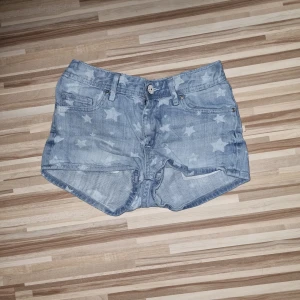 Jeansshorts med stjärnmönster - Ett par jeansshorts med stjärnmönster. Shortsen har en knapp och dragkedja framtill samt fickor både fram och bak. Från H&M i storlek 134