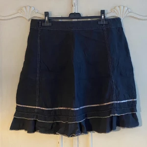 Svart Kjol - Svart kjol med fina volanger. Storlek 42 men skulle säga att den passar L-XL beroende på hur en vill att den ska sitta. Så fin och i bra skick men säljer för att den tyvärr inte kommer till användning. Hör gärna av dig om du har några frågor! 