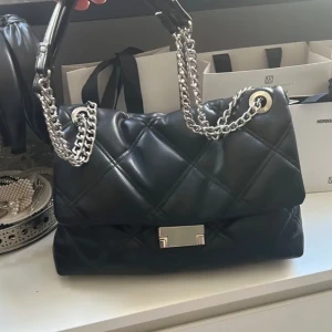 Svart puffig handväska - Så fin mellanstor handväska som får plats med mycket. Har ett fack i sig som är med dragkedja. Bra skick men lite använd. Från H&M men köpt i näst intill nyskick på Plick.