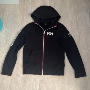 Helly Hansen hoodie - Helly Hansen hoodie till herr. Storlek S, sitter vanligt. Lite urtvättad samt ett litet slitage vid ena fickan(se bild 3).