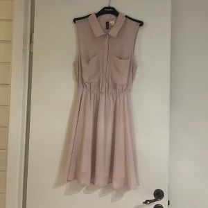 Klänning  - En fin blus klänning som passar de mer festliga aktiviteterna. Fin somrig färg av rosa. Har två fickor där framme med en fin krage och knappar.