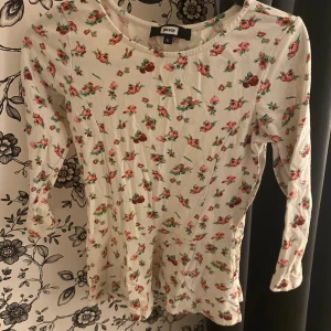 Blommig långärmad klänning från Bik Bok - Säljer en superfin blommig klänning från Bik Bok i storlek S. Klänningen är vit med ett sött blommönster i rosa och grönt. Den har långa ärmar och en rund halsringning. Perfekt för vår och sommar! 🌸