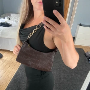 Brun väska - En brun handväska i imiterat krokodilskinn med gulddetaljer 