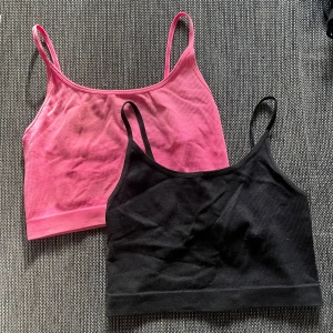 Två ribbade linnen i rosa och svart - Säljer två snygga ribbade linnen i storlek XS. Ett är i en härlig rosa färg och det andra är klassiskt svart. Perfekta för sommaren eller träning. Båda är ärmlösa med smala axelband och har en tight passform. De är i använt skick!🩷🖤