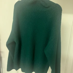 Stickad tröja  - Mörkgrön stickad tröja med mellanhög hals och slits i ärmarna från H&M i storlek M (passar även L). Endast använd 3 gånger och är därför lite nopprig. Annars utmärkt skick. Köpt för 350kr