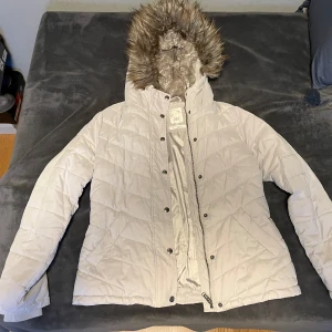 Beige vinterjacka - Säljer en elegant beige vinterjacka från märket 365, köpt på MQ. Jackan har en värmande huva med stilfull pälskant och är i storlek 38. Den är i mycket fint skick och har endast använts ett fåtal gånger.