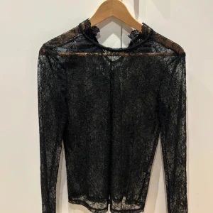 Svart spetsblus - Säljer en elegant svart spetsblus med långa ärmar. Blusen är genomskinlig och har en hög hals med fina spetsdetaljer. Perfekt för en festlig kväll eller en stilfull dag på jobbet. Köp direkt eller ge prisförslag 💛