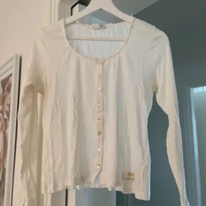 Vit långärmad kofta från Odd Molly - En vit långärmad tröja från Odd Molly med knappar framtill. tröjan har en rund halsringning och en lätt ribbad struktur. 