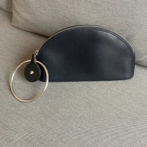 Kuvertväska - En lite speciell kuvertväska eller festväska från Don Donna med silverring att sätta runt handleden. Använd en gång. Små märken från annan väska som legat emot den. Mått: höjd 14cm, bredd 23cm, djup 5cm i botten. 