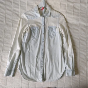 Ljus/blekt jeansskjorta/skjorta med knytband/skärp - Ljus jeansskjorta/bomullsskjorta i en annorlunda ojämn "blekt" färg. Ett par ljusare prickar/fläckar. En lite längre modell, med knytband. 