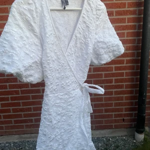  Vit omlott klänning med blommönster på🌸  - Klänningen är köpt sen nåt år tillbaka och säljs pga att den inte används. Har använt klänningen ett fåtal gånger. Därav är klänningen i väldigt gott skick. Ganska säker på att den är köpt från vero Moda. Köpare står för frakten💕