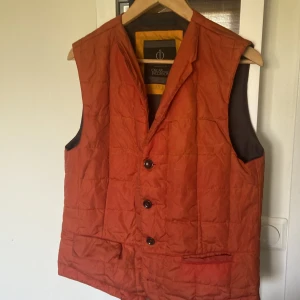 Trendig väst - Trendig orange väst från Oscar Jacobson i runt material. Storlek 48/M (passar nog även small). Säljes pga passar inte längre.