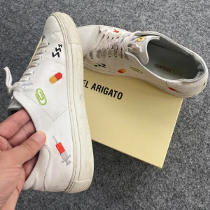 Axel Arigato Clean 90 Emoji (låda etc. inkluderat) - Axel Arigato skor Clean 90 Emoji Sneaker White Leather. Feta handgjorda skor som inte finns längre. Axel Arigato låda + påse + ätpinnar är inkluderat! Köpt på caliroots. Använt skick men ändå stabila. Storlek: 42 EU. Hör av er vid eventuella frågor!!