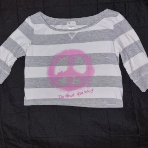 Randig tröja med rosa tryck - En randig tröja med grå och vita ränder. Tröjan har ett rosa tryck med ett fredstecken och texten 'Do what you love!' på framsidan. Den har trekvartsärmar och en rund halsringning. Från R teens i stl 146/152