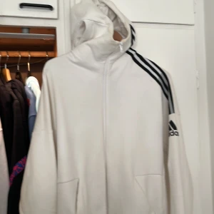 Träningskofta från Adidas - En knappast använd träningskofta/ vanlig kofta från Adidas som behöver en tvätt, har blixtlåsta fickor, luvan och toppen av koftan täcker munnen vid kalla temperaturer, har halva vantar inbyggda