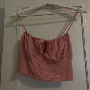 Rosa linnetopp från NA-KD - En rosa linnetopp från NA-KD med smala axelband och en knytning framtill. Toppen är tillverkad i Turkiet och har en avslappnad passform.