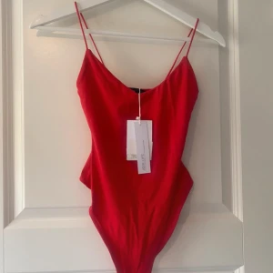 Bershka body XS - Röd body med dubbelt tyg vid brösten och 2 knappar ner. Den har string vid trosan och spagetti straps vid armarna. Helt oanvänd med prislapparna kvar. Passar även någon i S. Stretchigt tyg. Mer info hittar du i min bio 😊