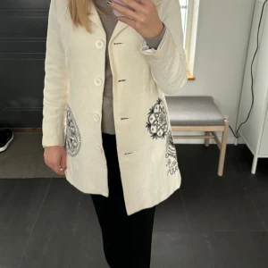 Creamvit kappa från Desigual, storlek 36. - Jättefin Kappa från märket Desigual som passar perfekt att ha till hösten och våren.  OBS! Mellan 27 juni till 1 augusti är jag bortrest och kommer inte att kunna skicka någonting då.