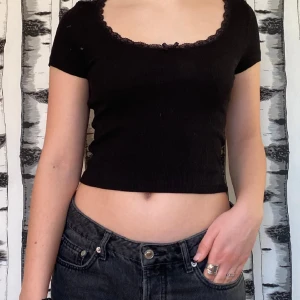 T-shirt  - Svart T-shirt från hm med spets i halsen och rosett längst fram. Lite kortare T-shirt perfekt till både vardag som fest😍