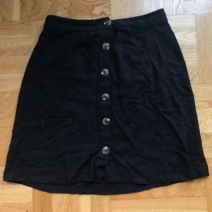 Svart kjol - Säljer denna svarta kjol med knappar då den inte är min stil längre. Den är i mycket skönt och svalt material och passar perfekt till sommaren, men även vår och höst. Köparen står för frakt. 