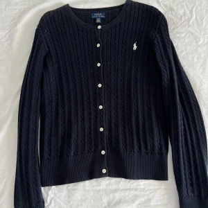 Kabelstickad kofta ralph lauren - Marinblå kabelstickad kofta från ralph lauren som är jättefin och söt att bara slänga över exempelvis en klänning eller ett linne. Bra skick och sitter som en storlek XS