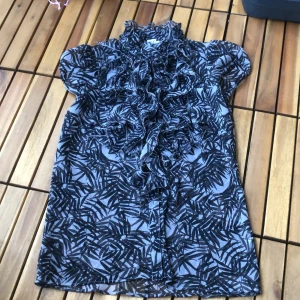  - Topp/blus med skirt tyg, krås och knäppning fram. Nedre knappen saknas. 